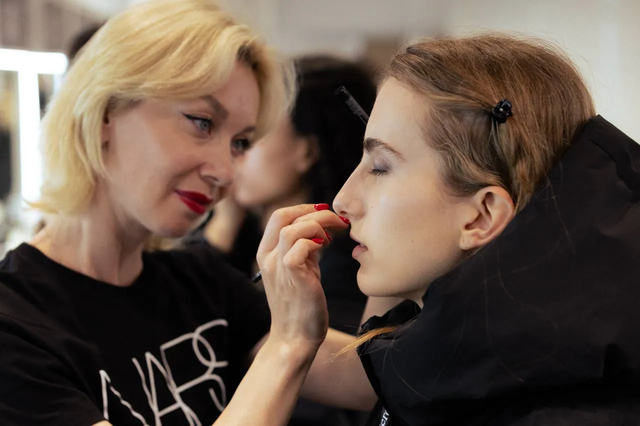 Екатерина в футболке NARS наносит макияж модели за кулисами показа