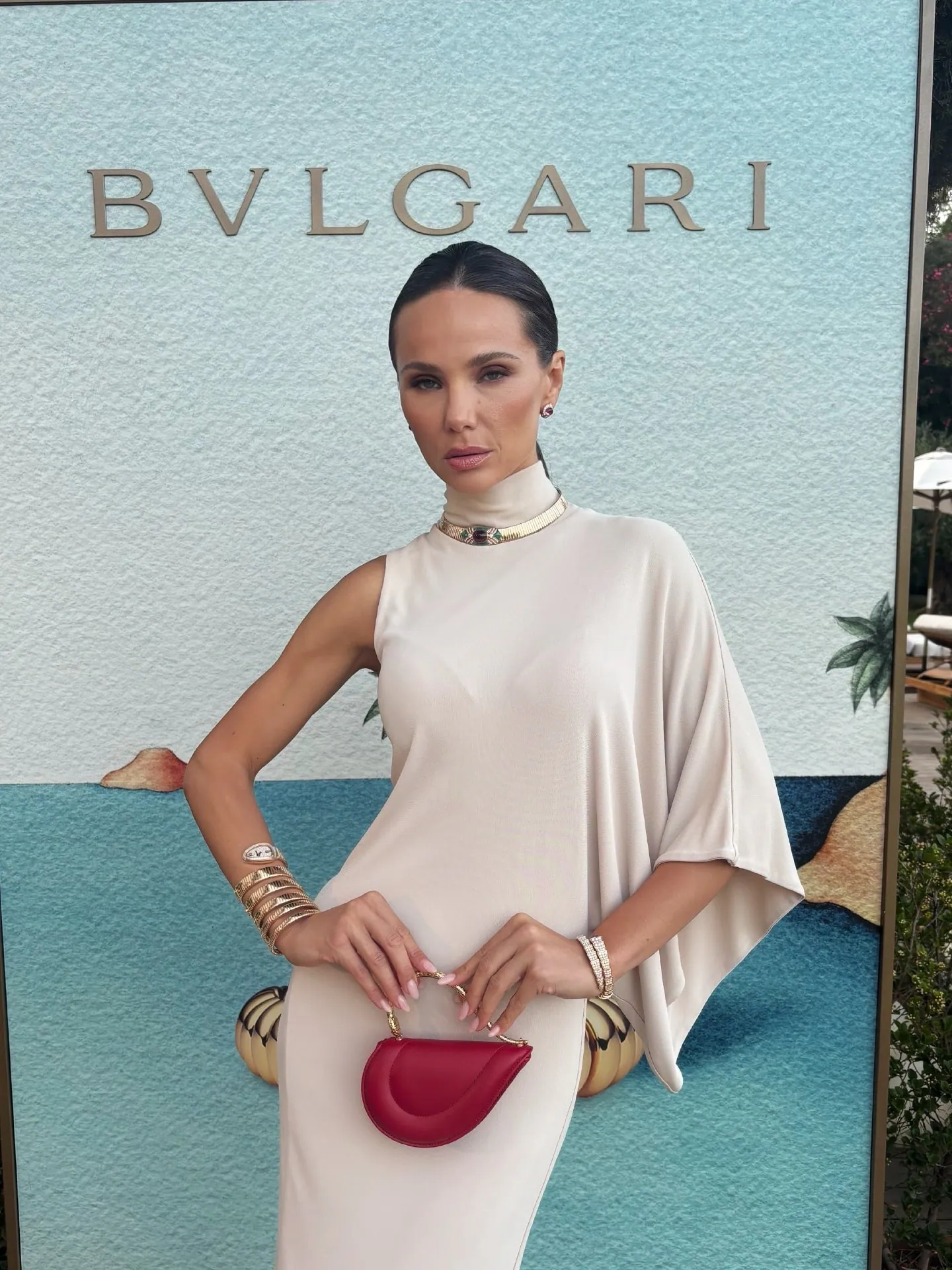 Модель в кремовом шёлковом платье с украшениями Bvlgari у брендового задника показа
